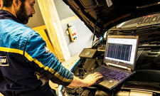 Mechaniker beim Chiptuning mit Laptop vor dem Motor bei geöffneter Motorhaube