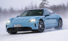 Das Porsche Taycan 4 Facelift (2025) driftet im Schnee durch eine Linkskurve, von vorne links fotografiert.