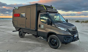 Greenlander Sherpa 4x4 (2024) steht am Sandstrand, Meer im Hintergrund, Fahrzeug von vorne rechs fotografiert.