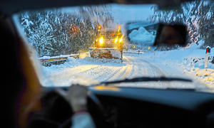 Ein Auto fährt einem Schneepflug entgegen in verschneiter Landschaft.