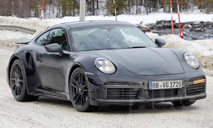 Der als Erlkönig getarnte Porsche 911 Turbo S Facelift (2024) fährt auf einer verschneiten Straße entlang.