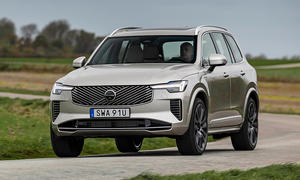 Das Volvo XC90 Facelift (2024) fährt über eine Landstraße, von schräg vorne fotografiert.