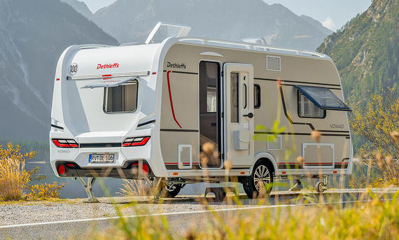 Dethleffs Nomad 490 EST (2025) am Straßenrand geparkt, die Tür ist geöffnet. Ansicht von hinten rechts. Im Hintergrund ein Gebirge.