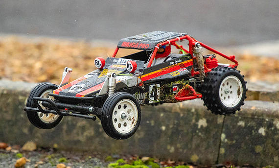 Das Bild zeigt den Tamiya Wild One fahrend von schräg vorne links fotografiert. Das RC-Auto springt über einen Bordstein.