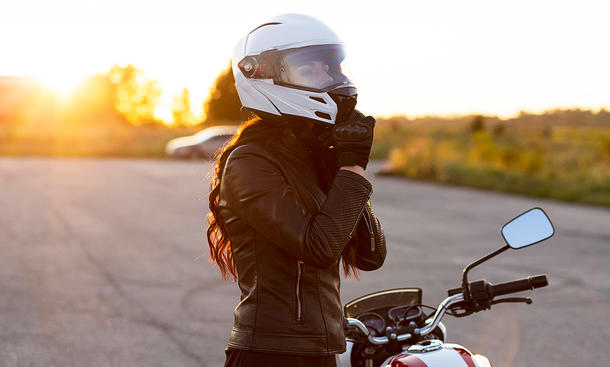 Eine Frau steht neben ihrem Motorrad auf einem leeren Parkplatz und schließt die Schnalle ihres Helms.