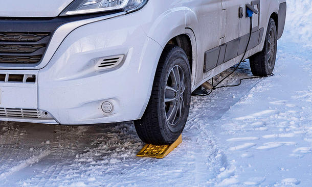 Auffahrkeile für Campingfahrzeuge: Symbolbild zeigt Camper im Schnee mit Vorderrad auf Auffahrkeil.