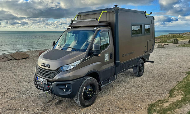 Greenlander Sherpa 4x4 (2024) steht auf einem Sandstrand, Meer im Hintergrund, Fahrzeug von vorne links fotografiert.