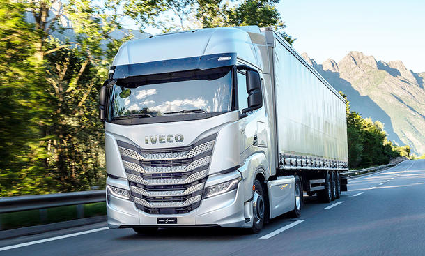 Der Iveco S-Way (2024) fährt über eine Landstraße mit malerischem Bergpanorama, von vorne fotografiert.