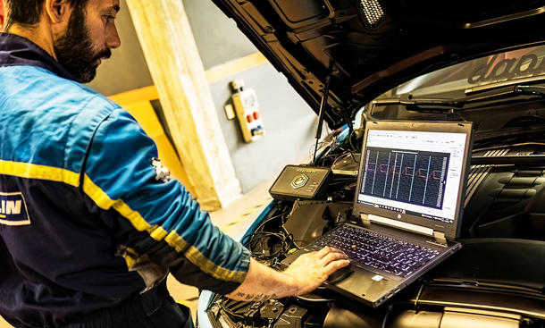 Mechaniker beim Chiptuning mit Laptop vor dem Motor bei geöffneter Motorhaube.