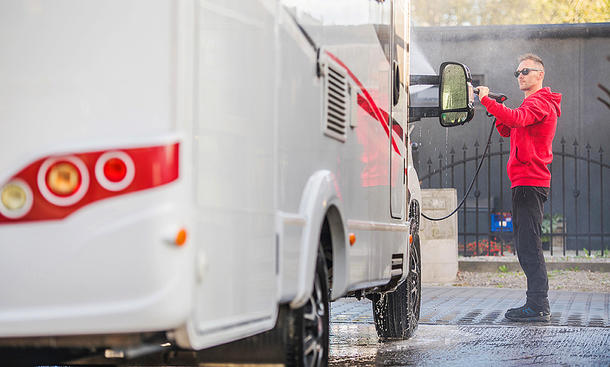 Das Bild zeigt eine Person, die mit beiden Händen einen Hochdruckreiniger hält und ein Wohnmobil mit dem Wasserstrahl reinigt.